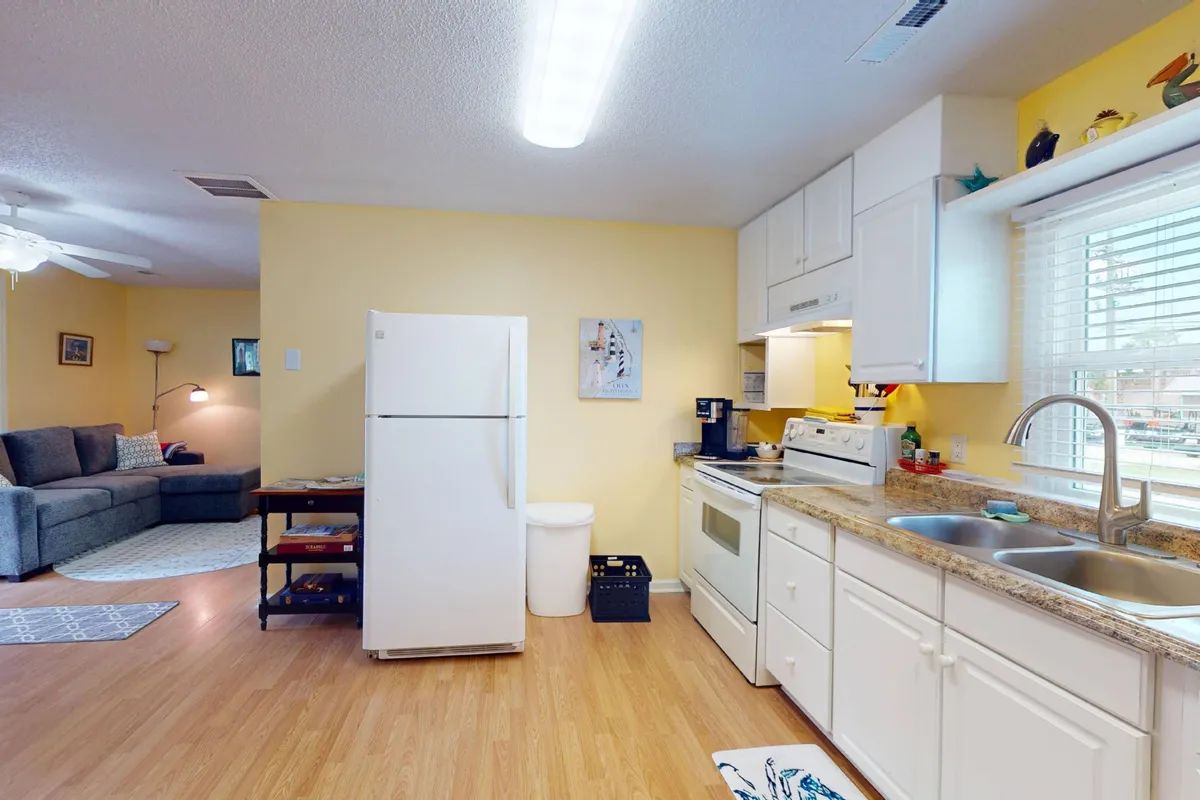 A bright, inviting kitchen opens out to a cozy living area. Stainless steel appliances, a generous countertop, and a comfortable sofa are visible, suggesting a space ideal for cooking, entertaining, and relaxing as a group.