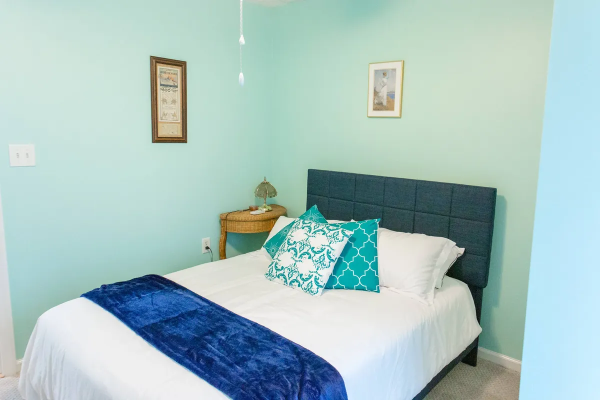 A cozy, softly lit bedroom interior with a plush king bed adorned with decorative pillows, a nightstand with a lamp, and tasteful artwork on the wall. The ambiance is inviting and serene, ideal for unwinding after a day of exploration.