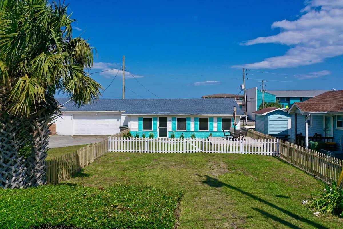 A brightly colored house with a white picket fence and lush palm tree sits in the foreground, providing a clear view of the fenced yard. The inviting space offers privacy and security, making it ideal for pets and outdoor activities.